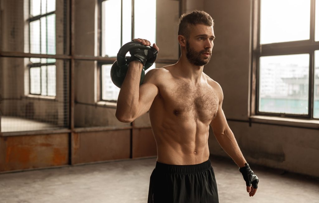 Shirtless man working out with kettlebell